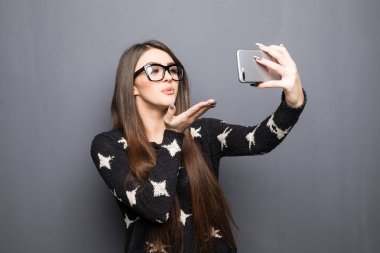 Genç güzel kız bir selfie yapma ve gri arka plan üzerinde bir öpücük gönderme
