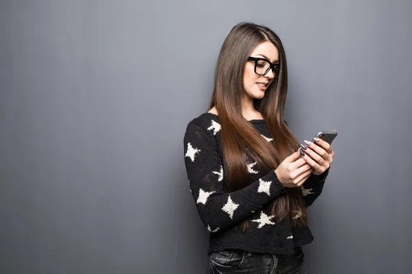 Bela jovem empresária segurando telefone celular e olhando para a câmera enquanto está de pé contra fundo cinza — Fotografia de Stock