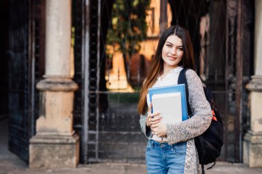 Genç ve güzel kadın öğrenci sırt çantası açık havada kampüs yakınında yürüyüş ile gülümseyen