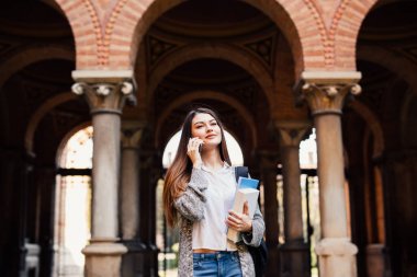 Üniversite kampüsünde telefon muhteşem mutlu öğrenci holding dizüstü konuşmak