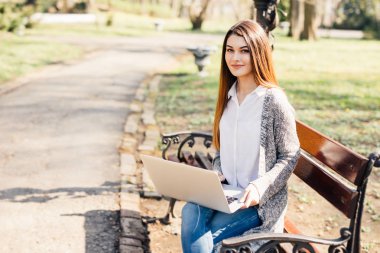 Parkta bir bankta bir dizüstü bilgisayar kullanan kız