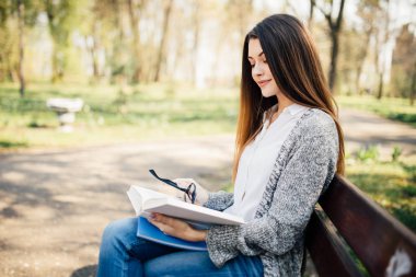 Çekici genç yetişkin kız öğrencinin banka açık havada park kitap okumak