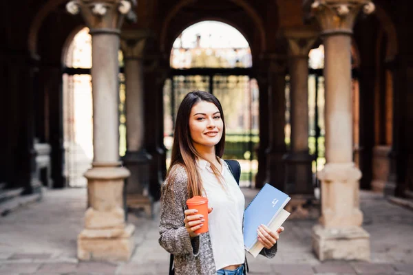 Jovem estudante de beleza com cadernos ao ar livre a universidade beber uma xícara de café — Fotografia de Stock