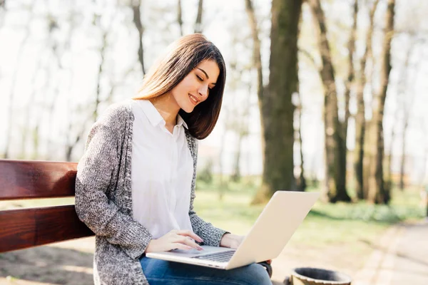 Молодая женщина работает на ноутбуке на скамейке в парке — стоковое фото