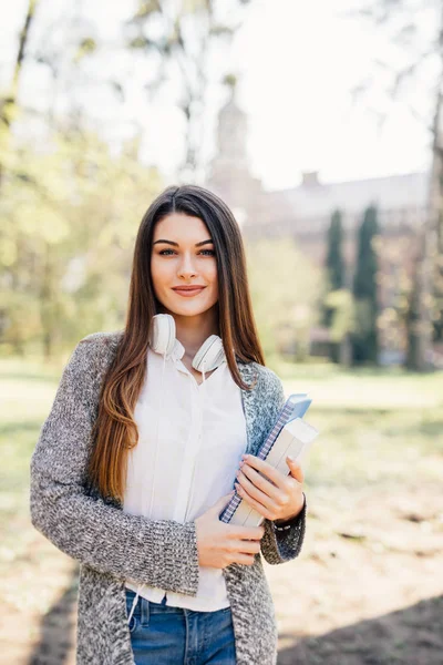 Jovem atraente alegre com cadernos de pé e sorrindo no parque — Fotografia de Stock