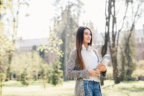 Universidade menina estudante universitário olhando feliz sorrindo com livro ou notebook no parque do campus. Mulher branca jovem modelo feminino . — Fotografia de Stock