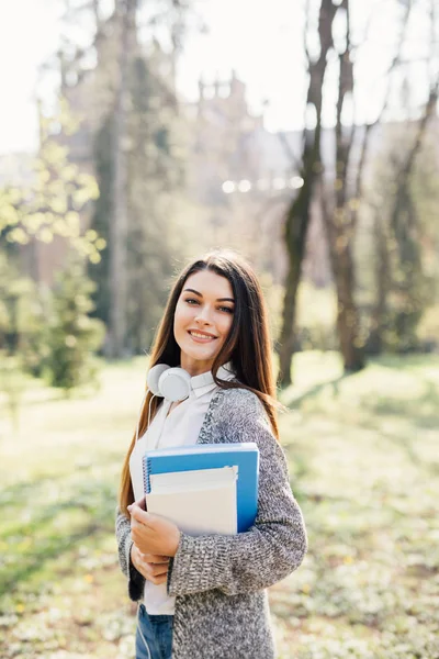 Студентка университета выглядит счастливой, улыбаясь с книгой или блокнотом в кампусе парка. Белая молодая женщина-модель . — стоковое фото