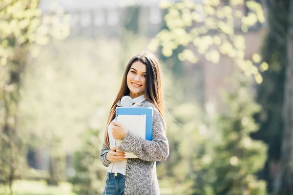 Jovem encantadora feliz de pé e segurando cadernos no parque — Fotografia de Stock