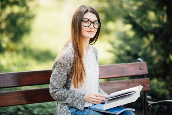 Una foto de un estudiante universitario leyendo un libro en el banco en el parque — Foto de Stock