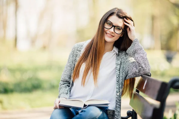 Šťastná mladá bruneta s notebookem v ruce, sedí na lavičce v parku — Stock fotografie