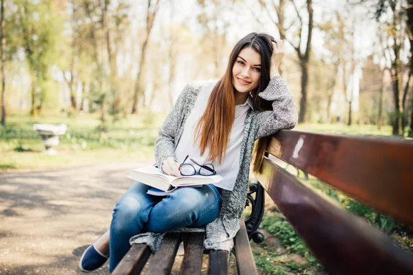 Dívka sedí na lavičce, čtení knihy slunečný den — Stock fotografie