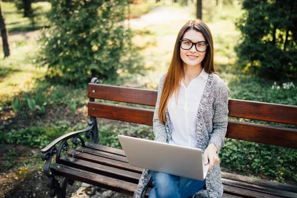 Молодая девушка на скамейке с ноутбуком в парке — стоковое фото