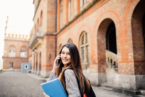 Single student walking and speak mobile phone with a university building in the background — Stock Photo, Image