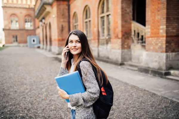 Single Student zu Fuß und sprechen Handy mit einem Universitätsgebäude im Hintergrund — Stockfoto