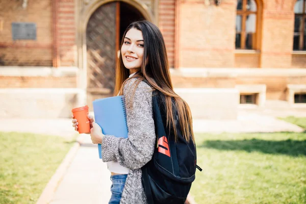 Американский студент улыбается с кофе и книжной сумкой в кампусе — стоковое фото