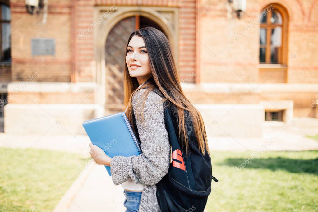 American university student smiling with coffee and book bag on campus