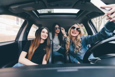 Selfie yapma ve arabaya birlikte otururken gülümseyen üç güzel genç neşeli kadın görünümünü