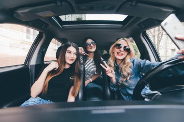 Selfie yapma ve arabaya birlikte otururken gülümseyen üç güzel genç neşeli kadın görünümünü