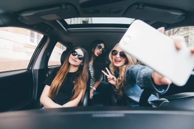 Selfie yapma ve arabaya birlikte otururken gülümseyen üç güzel genç neşeli kadın