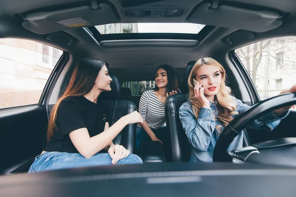 Dos hermosas jóvenes amigas hablando juntas en el coche o mientras van en un viaje por carretera conductor blanco hablar por teléfono — Foto de Stock