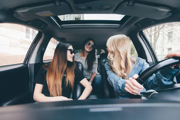 Viaje por carretera con bellezas. Vista de dos hermosas mujeres alegres jóvenes mirando hacia atrás a la tercera chica con sonrisa mientras está sentado en el coche — Foto de Stock
