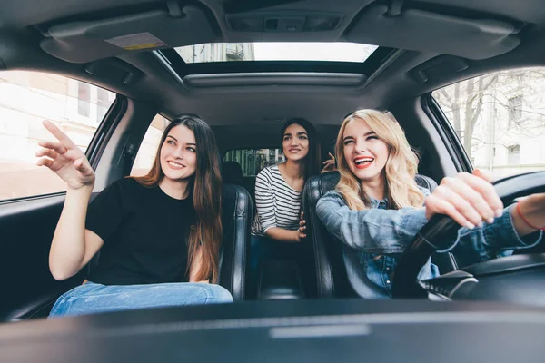 Три красивые молодые веселые женщины смотрят на заостренную руку с улыбкой, сидя в машине — стоковое фото