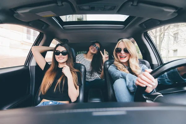 Tres hermosas mujeres alegres jóvenes mirándose con sonrisa mientras están sentadas en el coche — Foto de Stock