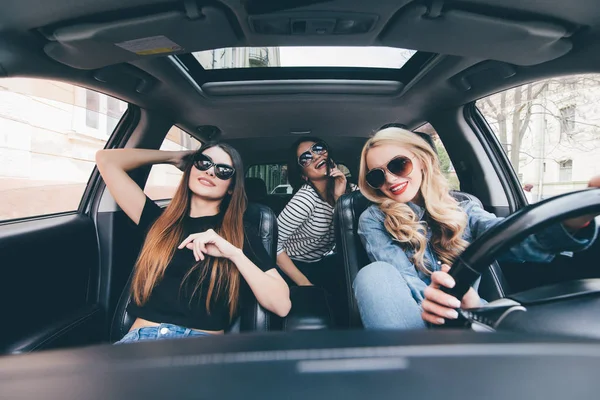 Три красивые молодые веселые женщины смотрят друг на друга с улыбкой, сидя в машине — стоковое фото