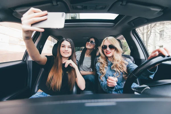 Група дівчат розважаються в машині і приймають селфі з камерою — стокове фото