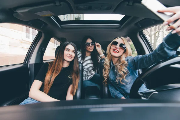 Selfie yapma ve arabaya birlikte otururken gülümseyen üç güzel genç neşeli kadın görünümünü