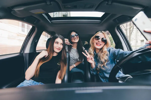 Weergave van drie mooie jonge vrolijke vrouwen selfie maken en glimlachend zittend in de auto samen — Stockfoto