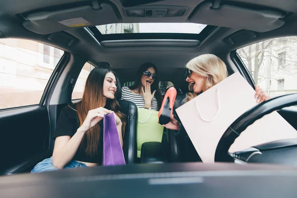 Tres mujeres se divierten y felices con las compras y los zapatos nuevos en el coche — Foto de Stock