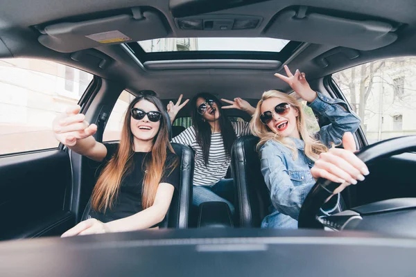 Три красиві молоді веселі жінки роблять селфі і посміхаються, сидячи в машині разом — стокове фото