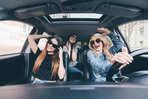 Три девушки едут в перевернутой машине и веселятся, слушают музыку и танцуют Стоковое Изображение