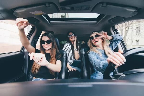 Три девушки едут в перевернутой машине и веселятся, слушают музыку и танцуют Стоковое Фото