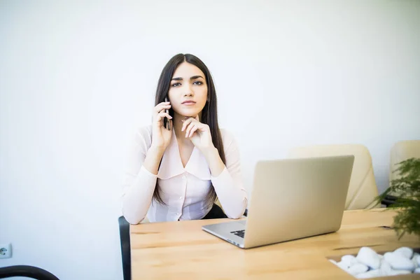 Retrato de la mujer financiera ejecutiva sentada en el escritorio y trabajando en el ordenador portátil mientras hace una llamada en la oficina — Foto de Stock