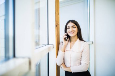 İş kadın konuşmak modern ofis içinde büyük ofis pencere eşiği telefon üstünde.