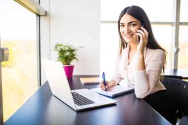 Mobil telefonda konuşurken ve ofis onun çalışma evinde oturan ve kameraya bakarak gülen çekici genç kadın