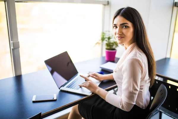 Joven hermosa mujer usando su computadora portátil mientras está sentada en la silla en su lugar de trabajo — Foto de Stock