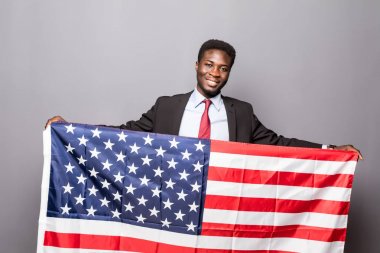 Klasik takım elbiseli yakışıklı Afro Amerikalı adam kameraya bakıyor ve Amerikan bayrağı ile ayakta gülümseyen