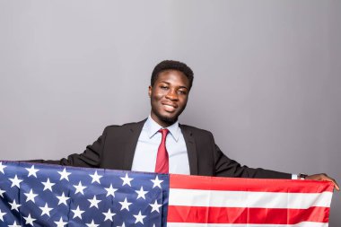 Klasik takım elbiseli yakışıklı Afro Amerikalı adam kameraya bakıyor ve Amerikan bayrağı ile ayakta gülümseyen