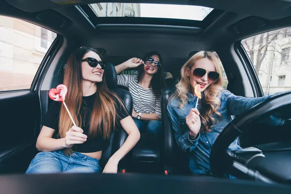 Три красивих молодих веселих жінки дивляться один на одного з посмішкою і їдять льодяники, сидячи в машині — стокове фото