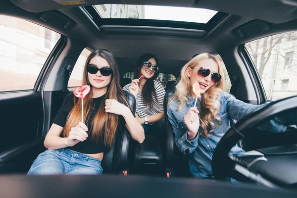 Чотири красиві молоді веселі жінки дивляться один на одного з посмішкою і їдять льодяники, сидячи в машині — стокове фото