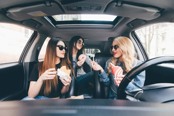 Троє молодих жінок їздять на машині, розмовляють один з одним і їдять фаст-фуду в машині в пробці — стокове фото