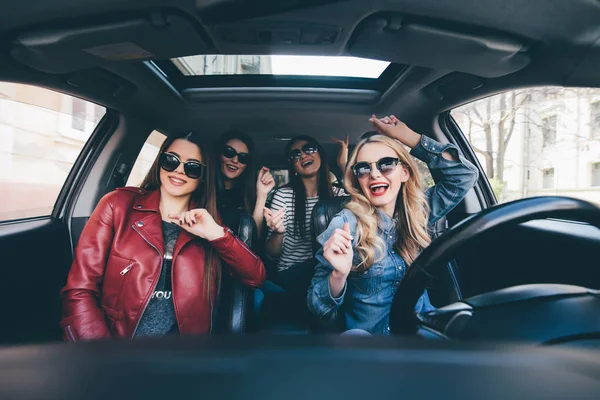 Чотири красиві молоді веселі жінки дивляться один на одного з посмішкою сидячи в машині — стокове фото