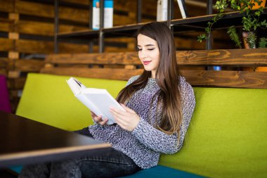 Genç kadın okuma kitabı kafe veya iş yerinde gülümseyen