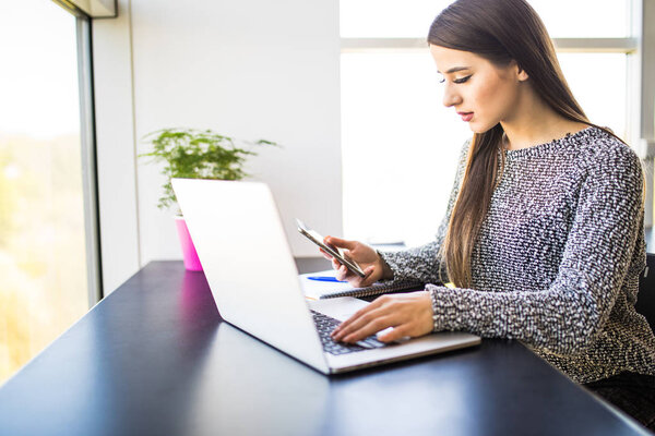 портрет красивой занятой женщины дома с помощью мобильного телефона и ноутбука в то же время в офисе
