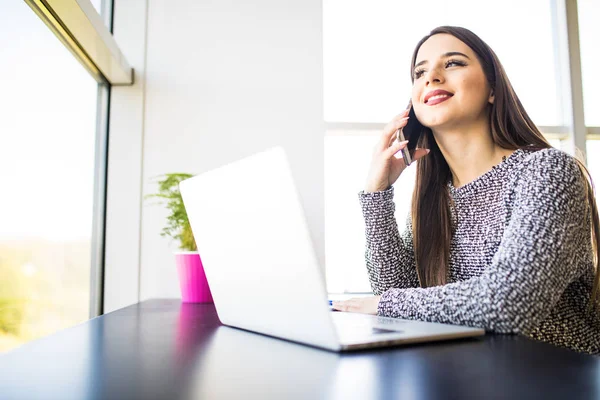 Hermosa mujer de negocios hablando por teléfono, trabajando con el ordenador portátil en la cafetería . — Foto de Stock