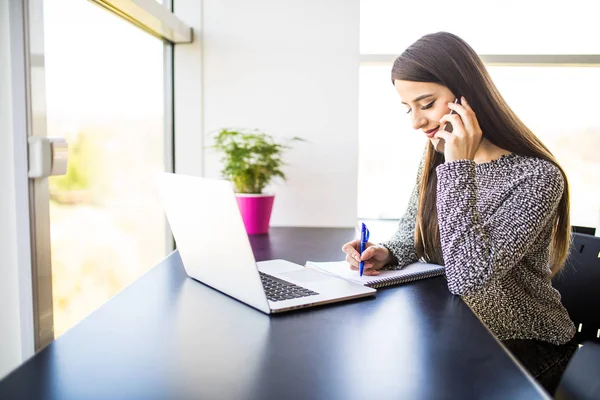 Freelancer kvinna arbetar på rad och prata i telefon och surfa i en bärbar dator hemma eller på kontoret — Stockfoto