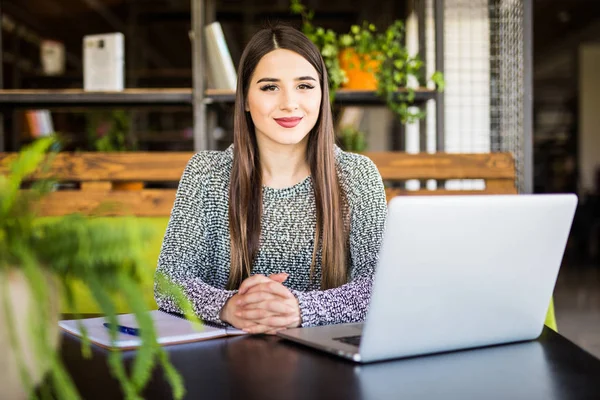 Joven mujer de negocios sentada en la mesa con el portátil y tomando notas en el cuaderno — Foto de Stock